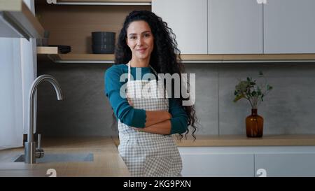 Jeune femme souriante femme de ménage femme maîtresse boulangère avec de longs cheveux bouclés portant un tablier à damier debout avec des bras pliés chef confiant Banque D'Images