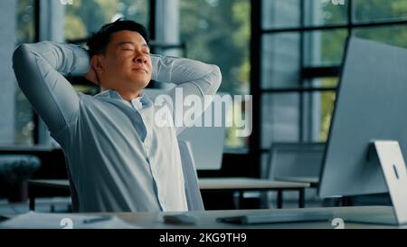 Un homme d'affaires asiatique coréen se détendant seul se pencher sur une chaise de bureau mettre les mains derrière le confort de la tête repos se sent satisfait par le travail informatique Banque D'Images