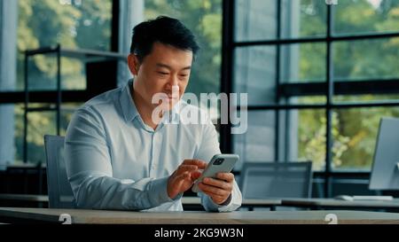 Excitée surprise gagnant homme d'affaires réussi asiatique mature japonais coréen homme chinois gagner surprise profitable offre en ligne Paris lecture bonne Banque D'Images