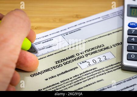 Main d'une personne qui remplit la déclaration fiscale annuelle au bureau fiscal de Pologne en 2023, formulaire de règlement pour les particuliers pour 2022 Banque D'Images