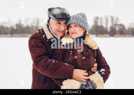 Portrait d'un couple de personnes âgées marchant à l'extérieur par temps hivernal enneigé. Des personnes mûres qui s'embrasent Banque D'Images