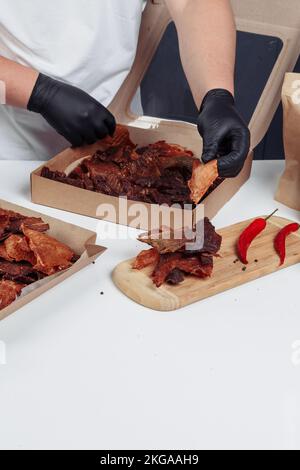 un gars met de la viande séchée dans des boîtes en papier dans des gants noirs Banque D'Images