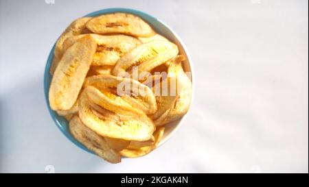 Chips de banane dans un bol bleu blanc sur fond blanc prêt à la vente Banque D'Images