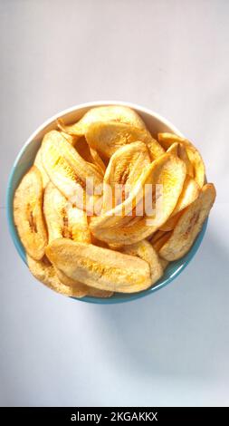 Chips de banane dans un bol bleu blanc sur fond blanc prêt à la vente Banque D'Images