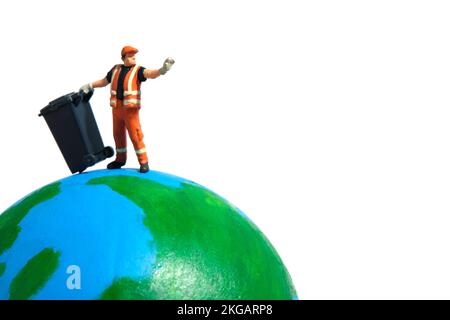 Travailleur de nettoyage avec une poubelle au-dessus du globe terrestre. Concept global de déchets. Photographie miniature de personnage Banque D'Images