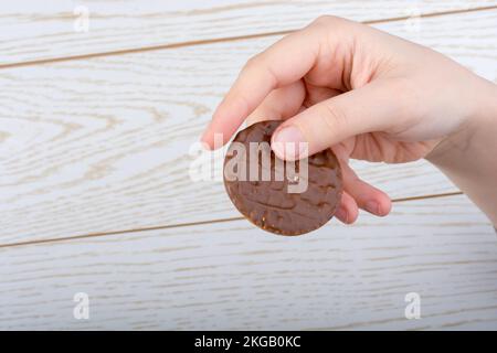 Main tenant un cookie recouvert de chocolat sur un fond de bois Banque D'Images