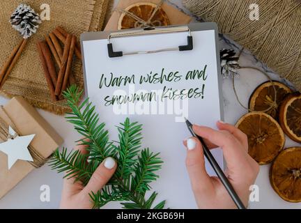 Voeux chaleureux et bonhomme de neige inspiration blague citation phrase femme faisant boîte avec les cadeaux du nouvel an, enveloppé dans du papier artisanal et décoré de branche de sapin. Concept de vacances et de cadeaux. Un Noël vert écologique fait main ne présente aucun gaspillage Banque D'Images