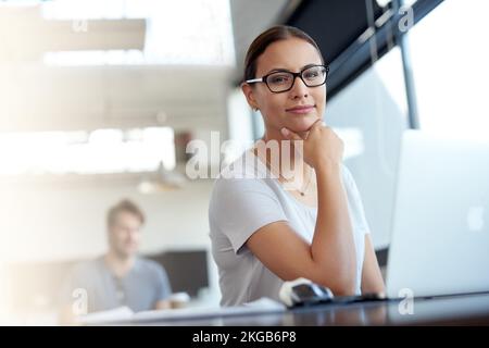 Elle est en avance sur les autres membres de cette entreprise. Portrait d'une jeune femme travaillant sur un ordinateur portable dans un bureau avec un collègue en arrière-plan. Banque D'Images