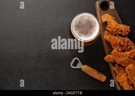 Une bouteille de bière sur une assiette avec des bretzels salés, des pistaches et des chips sur un tableau noir rayé. Vue de dessus. Photo de haute qualité Banque D'Images