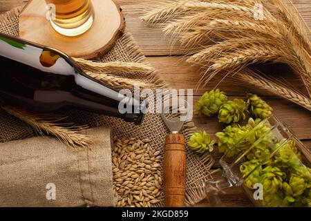 Une bouteille de bière avec houblon vert, avoine, épillets de blé, ouvre-bière et verres avec bière sombre et légère sur tableau noir rayé. Vue de dessus. Condition élevée Banque D'Images