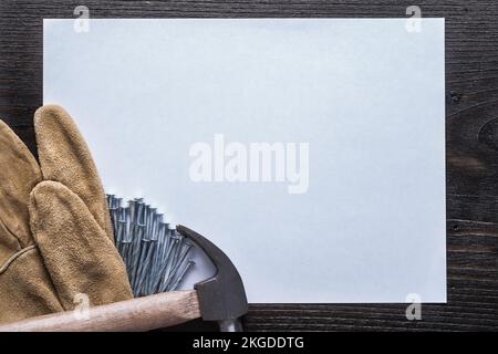 Feuille vierge de papier acier clous marteau et gants de protection en cuir sur panneau en bois vintage copier espace concept de construction. Banque D'Images