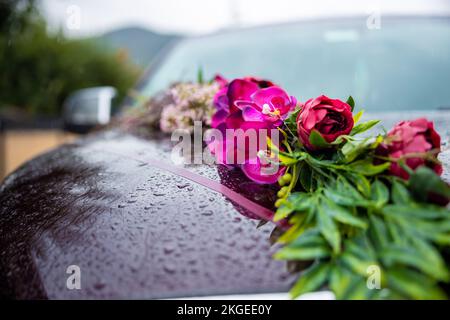 Belle voiture de mariage. Avant de la voiture de luxe décorée de fleurs roses par temps de pluie. Gouttes de pluie sur la voiture. Photo de haute qualité Banque D'Images