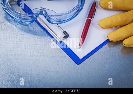 Lunettes de protection en plastique gants de sécurité stylo à bloc-notes sur fond métallique. Banque D'Images