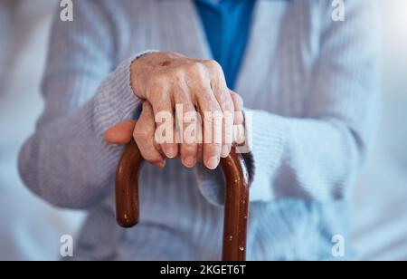 Les mains, la canne et l'incapacité avec une femme âgée de près dans sa maison seule avec un bâton de marche pour la mobilité. Santé, médecine et bien-être avec une maturité Banque D'Images