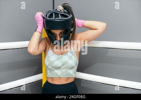 Femme mettant un casque de protection pour pratiquer la kickboxing debout dans le coin de la boxe Banque D'Images