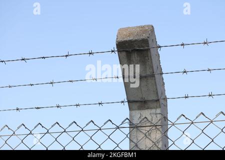 Clôture en barbelés de sécurité, fil avec des amas de pointes courtes et pointues sur le montant en béton Banque D'Images