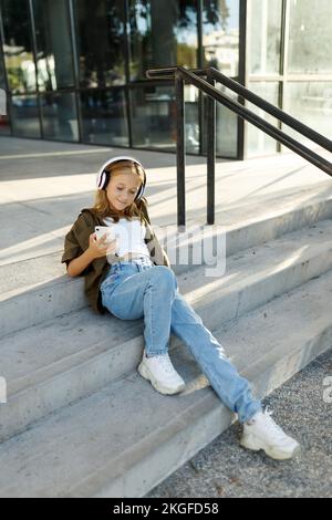 Jeune fille assise sur les escaliers de la rue le jour de l'été et ayant la conversation mobile sur le smartphone Banque D'Images