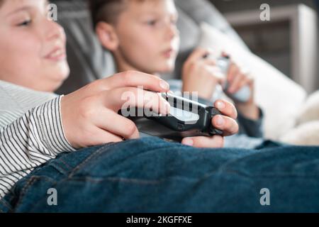 Vue latérale de deux adolescents allongé sur un canapé à la maison, tenant la manette de jeu manette de manette de jeu, jouant à des jeux vidéo sur la console. Passe-temps, gratuit Banque D'Images