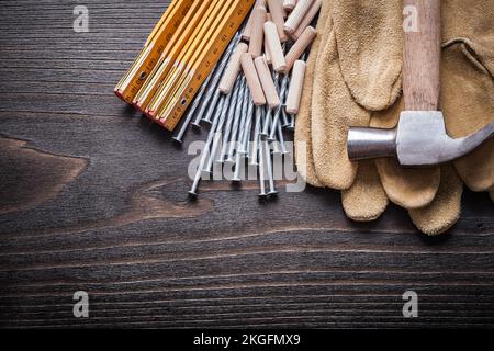 Pile de mètres en bois de chevilles à griffes marteau de gants de sécurité bruns et clous métalliques sur le concept de construction de panneaux en bois d'époque. Banque D'Images