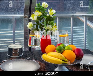 Table servie. Fruits frais et fleurs dans un vase rouge. Verres d'eau. Banque D'Images