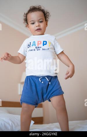 Drôle d'enfant heureux sautant sur le lit des parents dans la chambre principale Banque D'Images