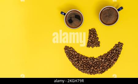 Émoticone souriant, lèvres en grains de café et yeux en tasses de café, composition sur fond jaune. Banque D'Images