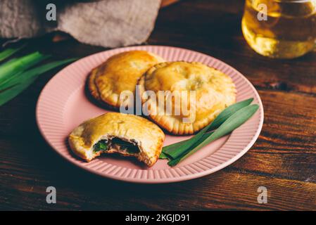 Tartes aux mains fraîchement cuites remplies de ciboulette et de champignons sur une assiette avec une tasse de thé vert Banque D'Images