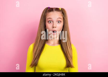 Photo de bonne humeur adorable écolière à queue de cheval vêtue jaune manches longues avec ouverture de la bouche isolée sur fond jaune Banque D'Images