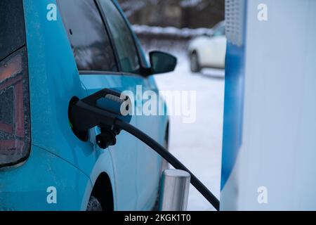 La fiche du chargeur est insérée dans la voiture électrique sur fond enneigé. Énergie verte. Banque D'Images