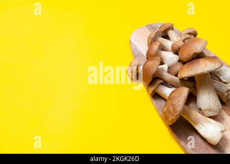 Capuchon marron Boletus edulis sur une planche à découper sur fond jaune. Champignons comestibles sur une planche en bois dans la cuisine. Personne Banque D'Images