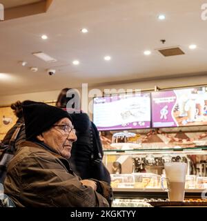Epsom, Surrey, Londres, Royaume-Uni, 20 novembre 2022, senior homme âgé avec Un café latte qui garde au chaud pendant la crise des coûts de chauffage au Royaume-Uni portant un chapeau de laine an Banque D'Images