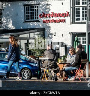 Epsom, Surrey, Londres, Royaume-Uni, 20 novembre 2022, petit groupe de personnes assis à l'extérieur parlant et boire du café avec AWoman Walking passé Banque D'Images