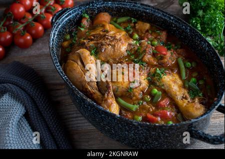 Ragoût de poulet brun avec légumes, pommes de terre et légumineuses dans un pot à l'ancienne sur table en bois Banque D'Images