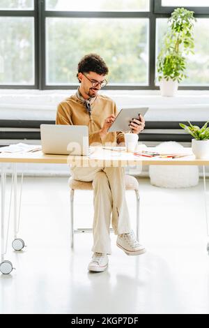 Graphiste souriant travaillant sur une tablette PC, assis au bureau Banque D'Images