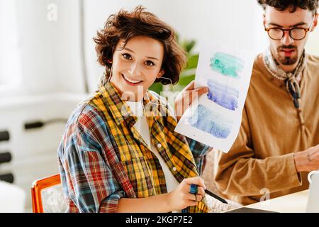 Heureux illustrateur montrant la peinture aquarelle par un collègue au bureau Banque D'Images