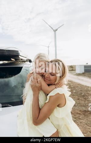 Femme souriante embrassant la fille assise sur le capot de la voiture Banque D'Images