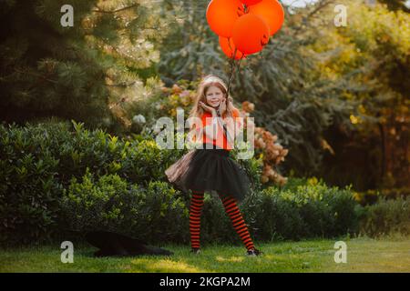 Fille souriante tenant des ballons orange debout avec la tête dans les mains à la cour arrière Banque D'Images