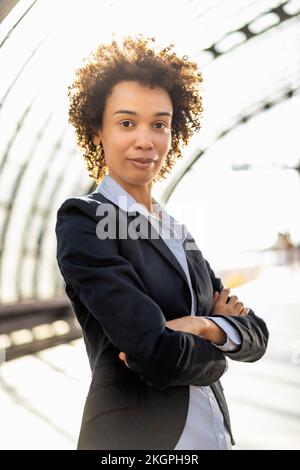 Femme d'affaires confiante portant un blazer debout avec les bras croisés à la gare Banque D'Images