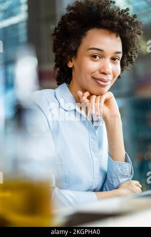 Femme d'affaires souriante avec main sur le menton au bureau Banque D'Images