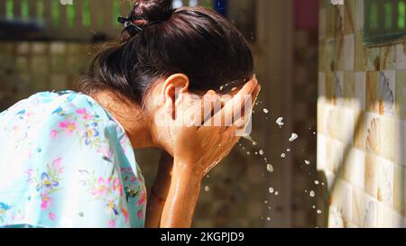 Belle femme est de laver le masque facial dans la salle de bains après avoir appliqué le masque facial. Fille pulvérisant de l'eau sur son visage debout devant le miroir à la maison. Boue Banque D'Images