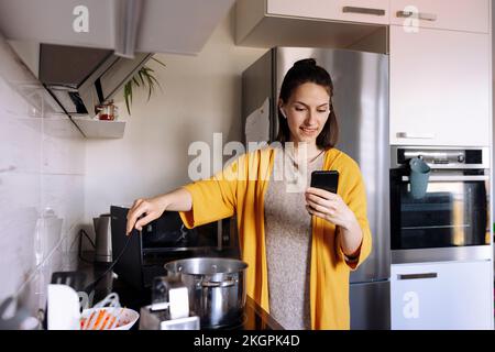 Femme en cuisine et en train de passer un appel vidéo via un smartphone dans la cuisine Banque D'Images
