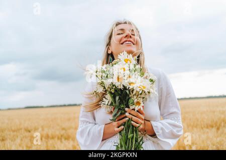 Femme souriante debout avec un bouquet de fleurs blanches devant le ciel Banque D'Images