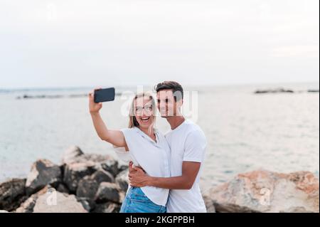 Couple heureux de prendre selfie sur téléphone portable à la plage Banque D'Images
