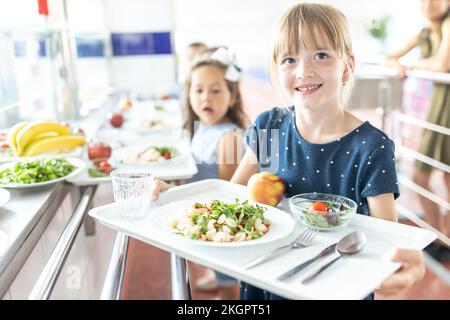 Une fille souriante tient un plateau à la pause déjeuner dans la cafétéria de l'école Banque D'Images