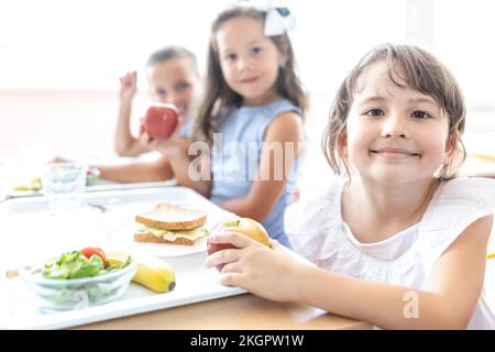 Un élève du primaire souriant avec un plateau à manger sur la table lors de la pause déjeuner à la cafétéria Banque D'Images