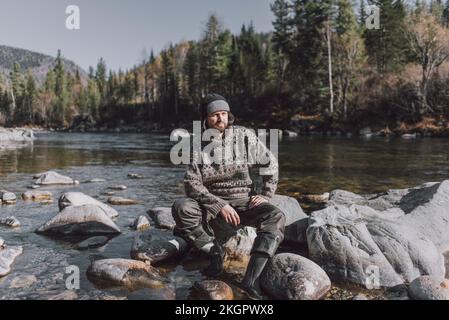 Homme contemplatif assis sur le rocher au bord de la rivière Banque D'Images