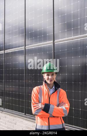 Femme ingénieure souriante avec bras croisés debout devant les panneaux solaires Banque D'Images
