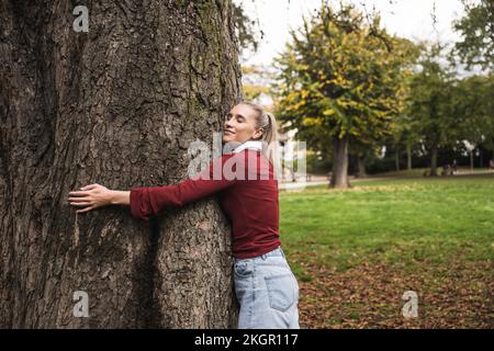 Femme souriante embrassant l'arbre au parc Banque D'Images