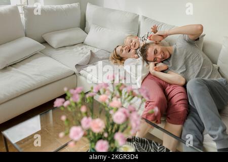 Mère et père heureux s'amuser avec leur fils sur le canapé à la maison Banque D'Images