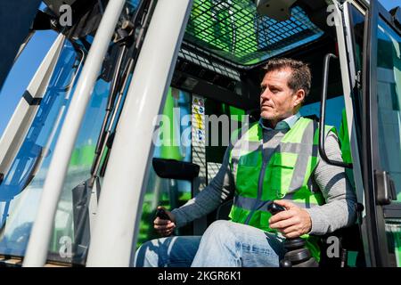 Homme utilisant une pelle hydraulique dans une usine industrielle par beau temps Banque D'Images